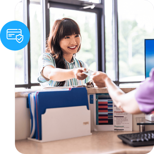 Customer handing a card across a counter with a blue card security icon overlay.