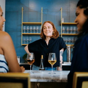 Three customers chat and drink wine at a bar.