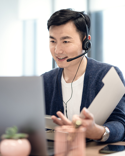 A customer service worker speaks to a customer while sitting at their desk, wearing a headset.