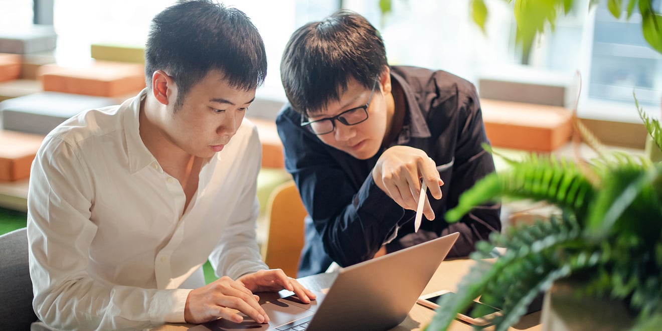 Two salesmen review their payment data on a laptop.