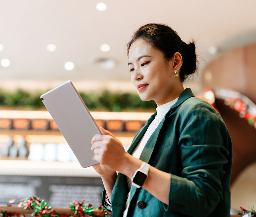 A person wearing a green blazer looks at information on a tablet while standing inside a business.