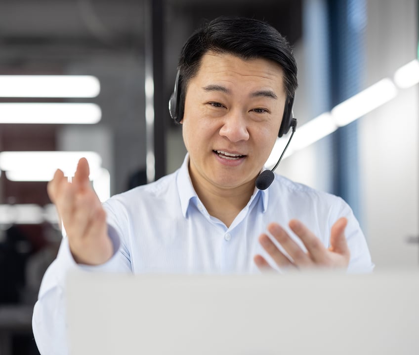 A customer service worker speaks to a customer while sitting at their desk, wearing a headset.
