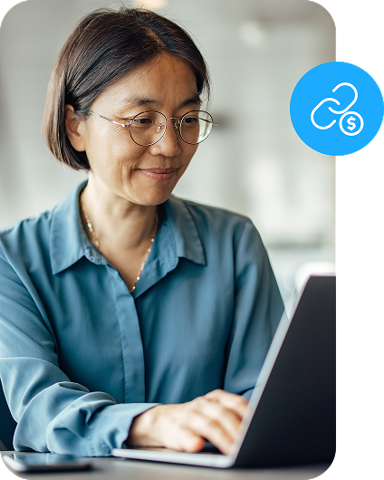 A woman sits at a table and works on a laptop while a pay by link icon in a circle sits atop the image.