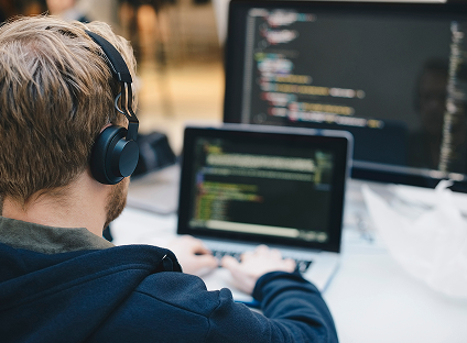 A person wearing headphones works at a busy desk on a laptop.