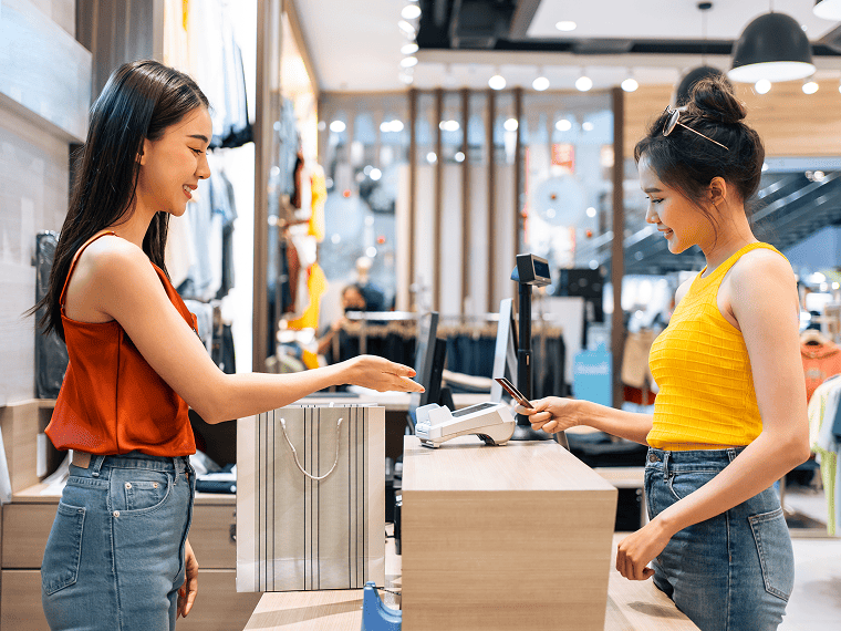 一位服裝店店員在收銀櫃檯為顧客結帳，顧客正以流動POS感應信用卡付款 一拍即付，成交更快 — 提升門店收款效率與顧客體驗。