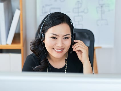 Smiling customer service rep wearing a headset and looking at a computer