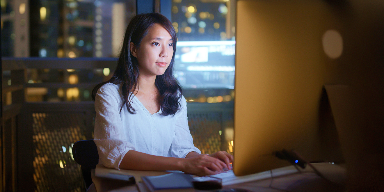 Person sitting in a dark room in front of a computer with the glow of the screen illuminating them
