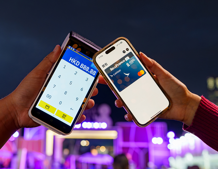 A hand holds a mobile phone with a tap to pay card showing as they tap another phone with a payment screen.