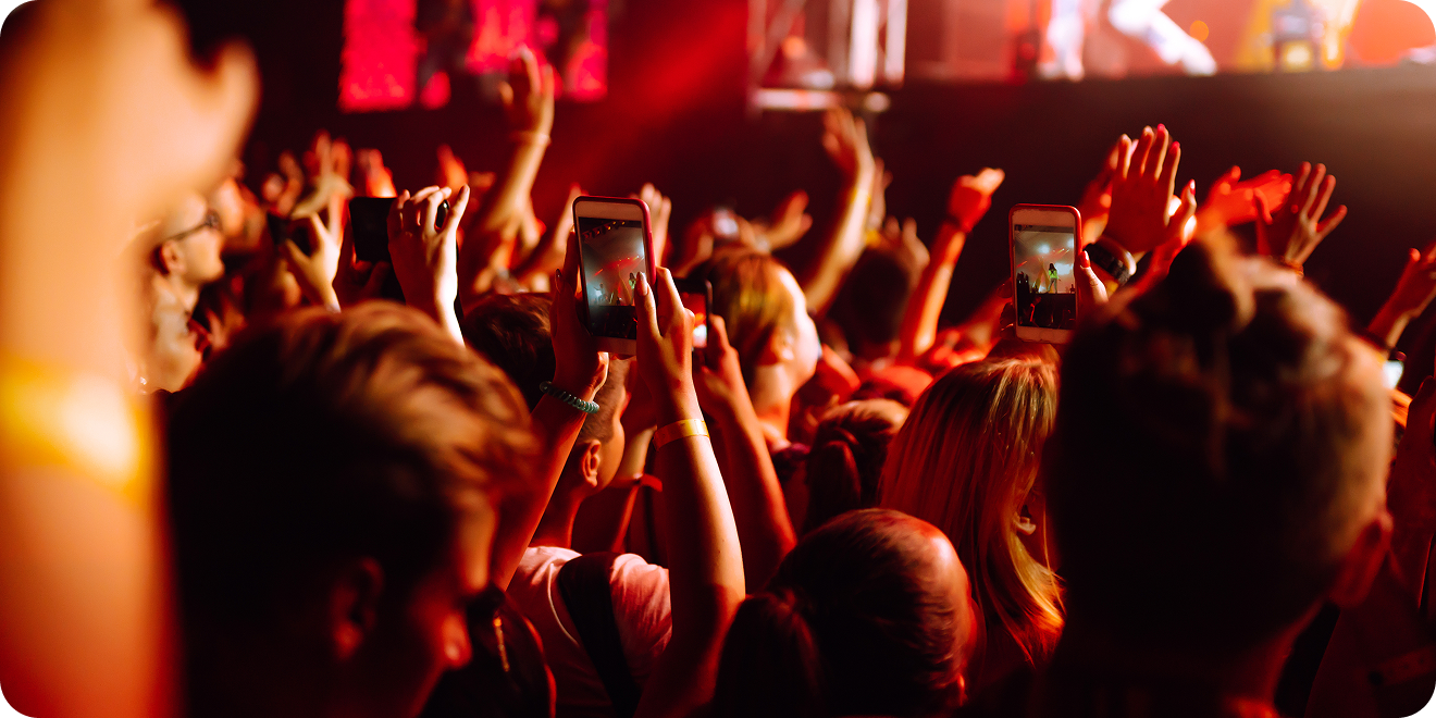 Fans in a crowd raise their hands while looking onto a stage during a performance at a venue.