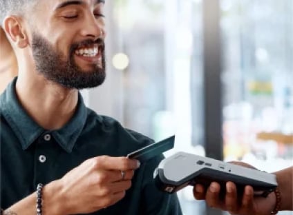 Smiling bearded man tapping a credit card on a POS terminal.
