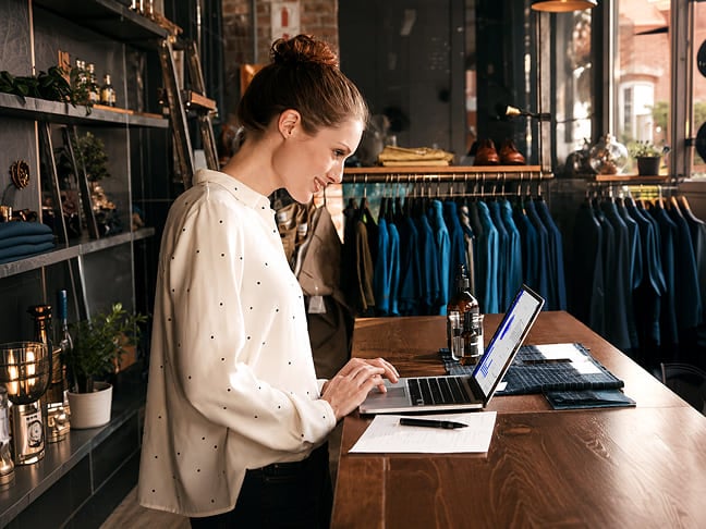 Retail store owner using a laptop at a counter inside her shop.