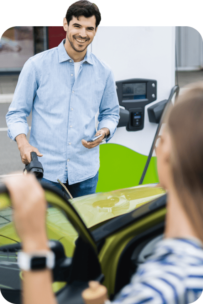 Man holding a smartphone and charging cable at an electric vehicle station.