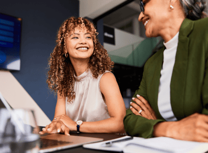 Two people smiling at each other while using a laptop in an office.