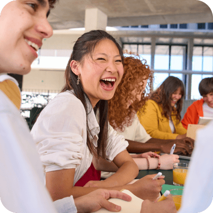Un groupe d'étudiants souriants et issus de divers horizons étudient et rient ensemble autour d'une table de classe.