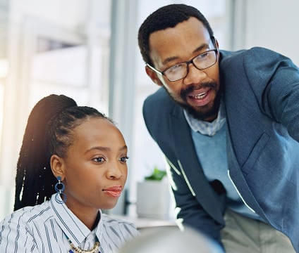 Un homme en blazer bleu et portant des lunettes montre un écran du doigt, tandis qu'une femme observe attentivement.