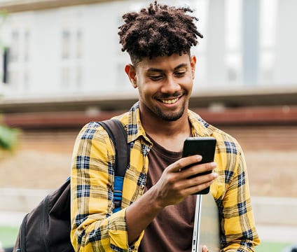 Un étudiant souriant tout en utilisant son téléphone portable sur un campus universitaire.