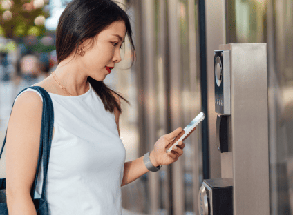  A woman uses her smartphone to scan an electronic door access reader outside a building.