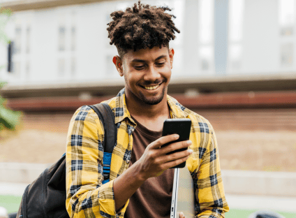 A student smiling while using their cell phone on a university campus.