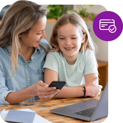 Une mère et sa fille sourient en regardant un smartphone à côté d'un ordinateur portable.