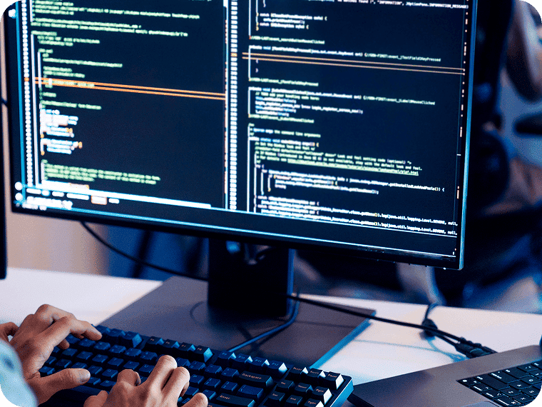 Hands typing on a keyboard in front of a monitor displaying lines of code.