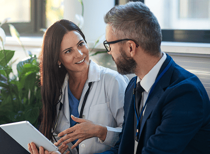 Smiling healthcare professional in a lab coat discusses data on a tablet with a colleague.