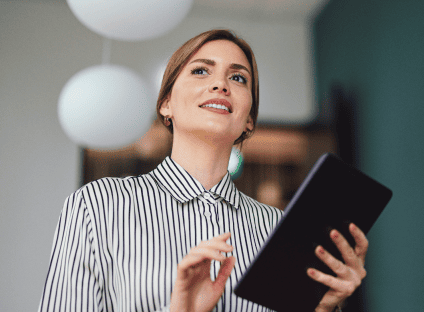 Smiling woman in a striped shirt holding a tablet and looking up thoughtfully.