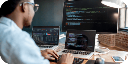 Un développeur travaillant à son bureau, avec des lignes de code et des graphiques affichés sur plusieurs écrans.
