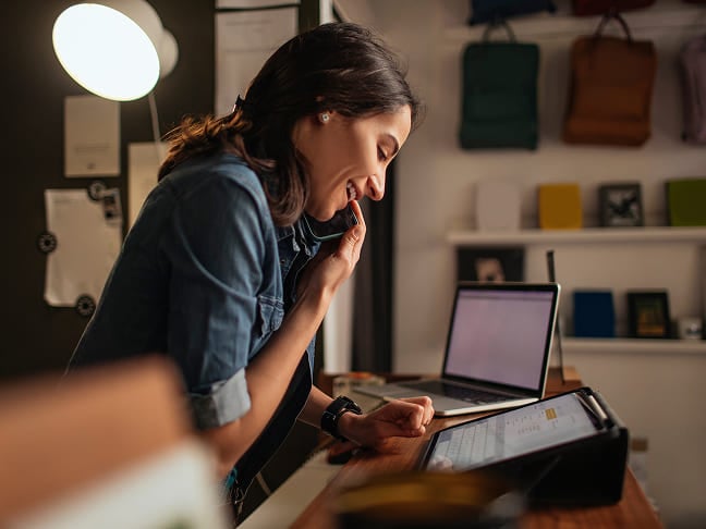 Woman smiling on a phone call while working on a tablet in her office.