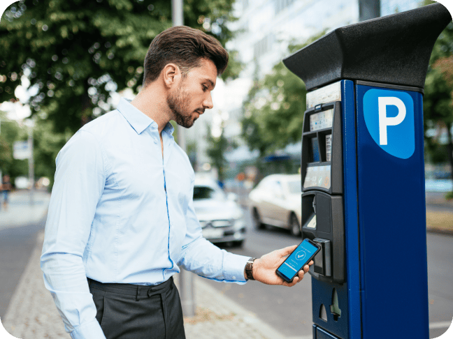 A man holds his mobile device in front of a parking payment terminal to perform an NFC transaction and reserve his parking space.
