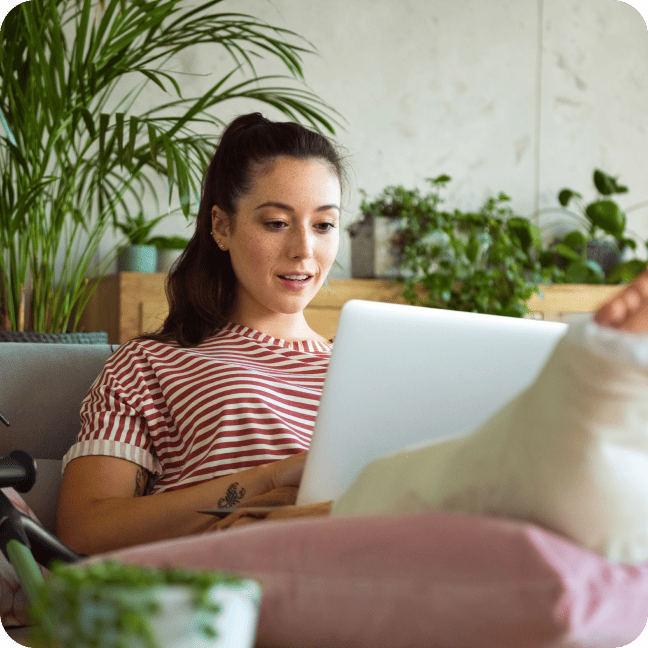 A woman with a cast on her foot sits with a laptop in her lap.