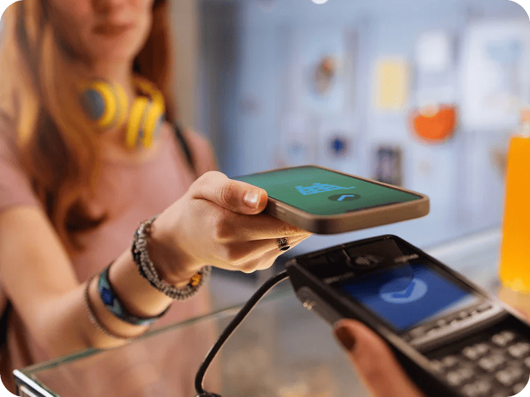 A person holds a smartphone near a card reader to make a contactless payment.