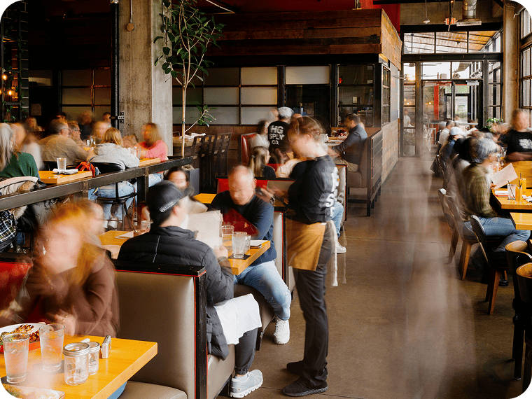 Serveur prenant les commandes des clients dans un restaurant animé et bruyant.