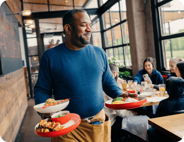 Un serveur de restaurant jongle avec plusieurs assiettes tout en servant les clients.