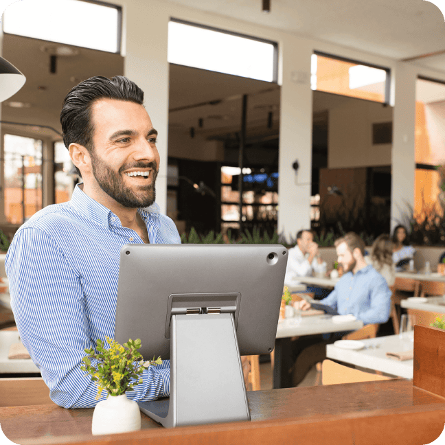 Un employé de restaurant en chemise rayée sourit derrière un terminal de point de vente.