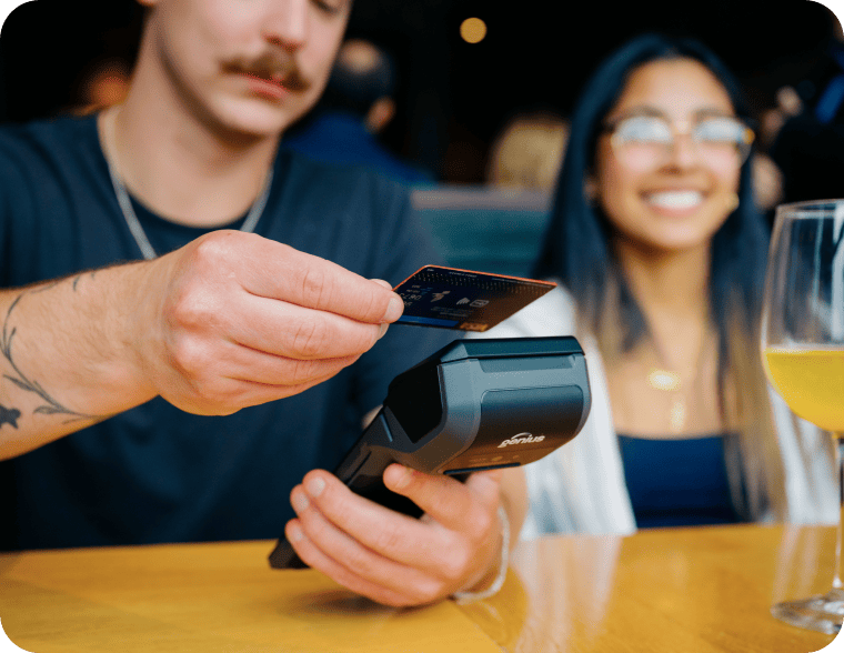 Man using a contactless card on a payment reader beside a smiling companion.