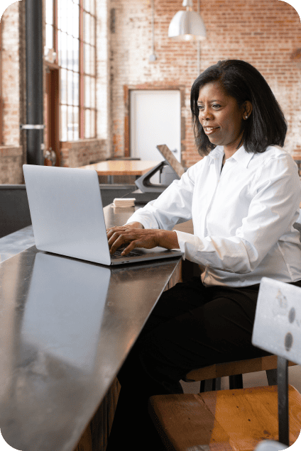 Woman in a white shirt working on a laptop at a high counter in an office.