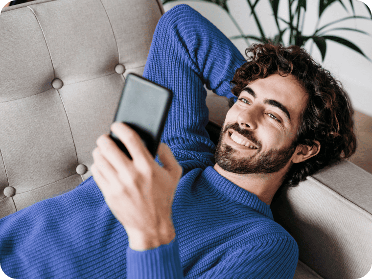 Man in a blue sweater reclining on a couch and using his mobile
