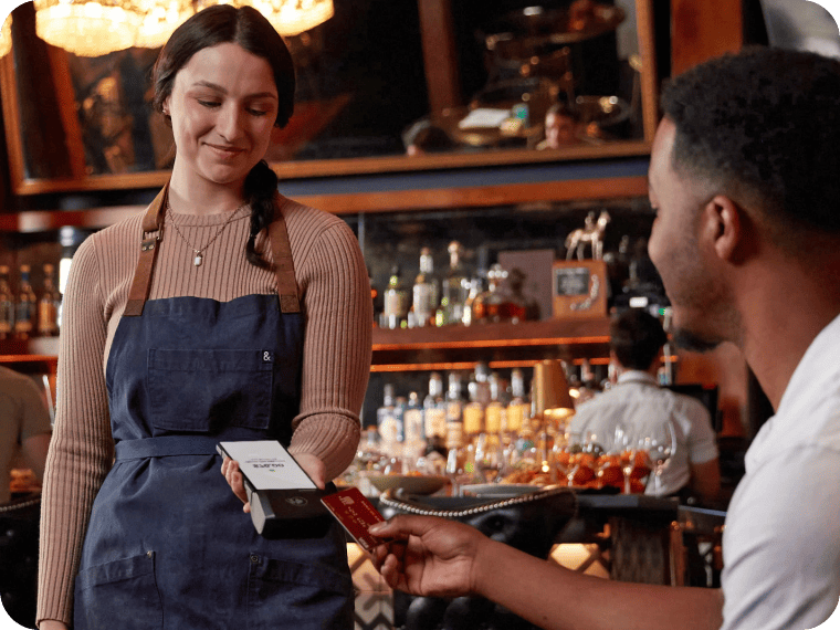 Server accepting a credit card payment with a handheld POS terminal at a restaurant.