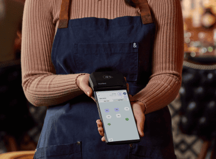 Restaurant staff holding a mobile payment terminal showing a table layout screen.