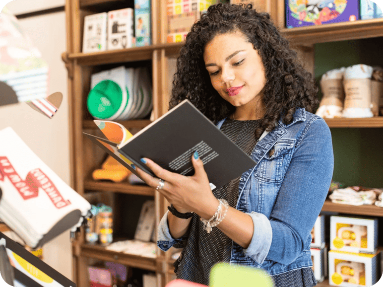 Woman standing near store shelves reading an open book.