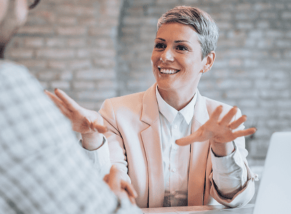 Woman in business suit sitting in front of a laptop and smiling while talking with her hands 