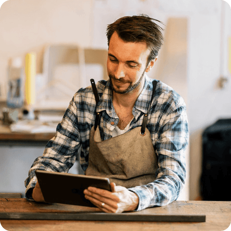 Small business employee wearing an apron, sitting at a table and looking down at a Genius tablet point of sale