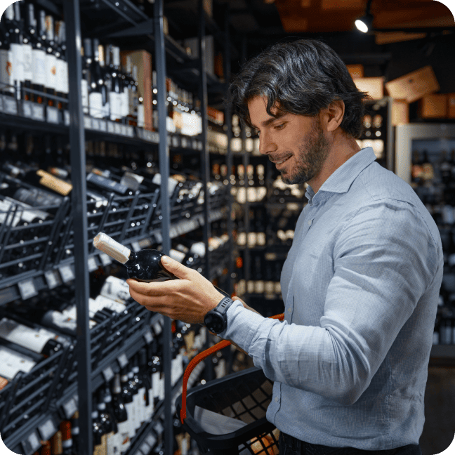 Homme examinant une bouteille de vin dans une allée de magasin pleine de bouteilles de vin.