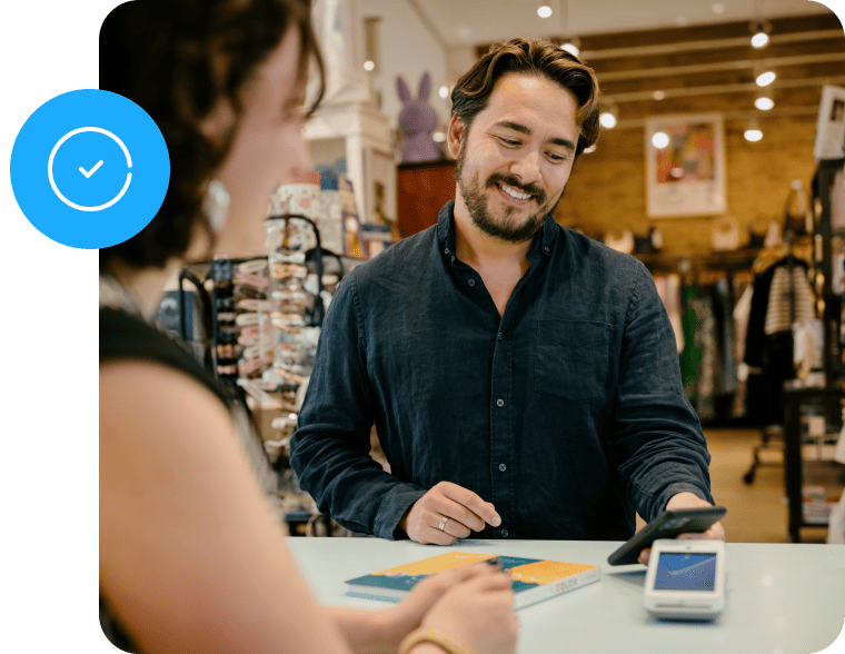 A man at a store counter uses his smartphone to make a payment, while a woman stands across from him.