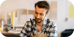 Man in a plaid shirt and apron looking down attentively in his creative studio.