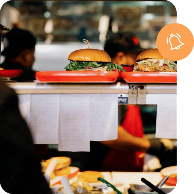 Food counter showing a line of tickets and two sandwiches on trays ready for pickup