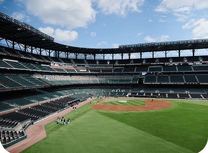 Empty baseball stadium field with green grass, dirt infield, and stadium seating.