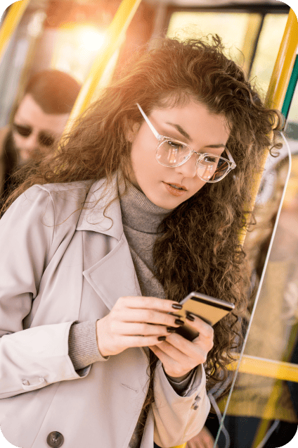 Woman wearing glasses and trench coat looking at her phone on a bus or train.