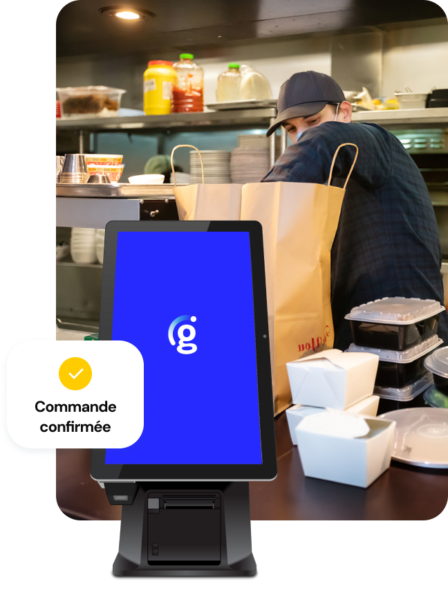 Vue d'une cuisine animée où une personne empile des contenants à emporter dans un grand sac en papier brun ; une borne Genius avec un petit message d'interface utilisateur indiquant « Commande confirmée » se trouve au premier plan.