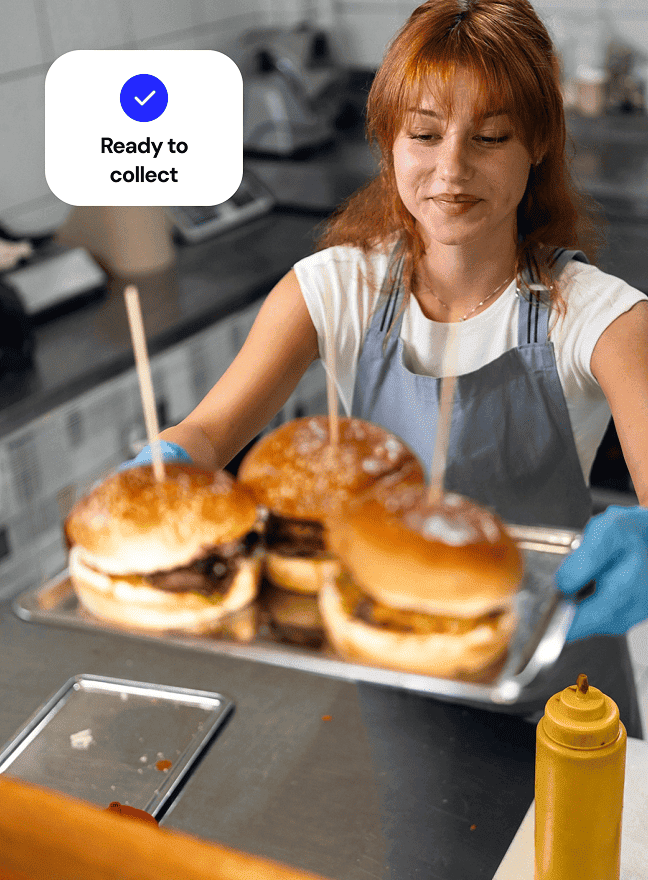 Restaurant kitchen worker serves up plate of burgers to server.